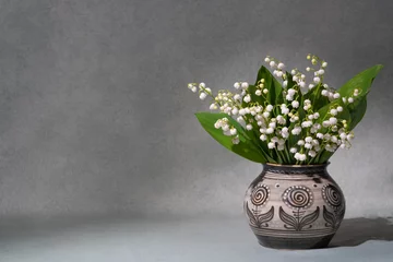 Zelfklevend Fotobehang A small bouquet of fresh spring flowers. Lilies of the valley in a light vase isolated on a gray background. Lots of space for text. still life, postcard, gift © Alexander