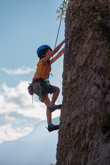 The child is climbing on a natural terrain. A boy climbs a rock on a background of mountains....