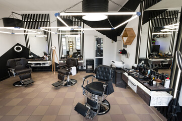 The modern interior of a mens barbershop with chairs is shot at a wide angle. Designer interior of a hair salon in black and white colors with LED lamps.