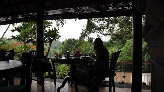 Woman looking at her phone while having breakfast in the restaurant hotel. Bali, Indonesia. High quality FullHD slow motion footage.