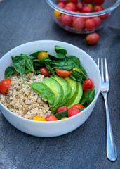 A dish of rice, avocado, tomatoes, and spinach next to a fork