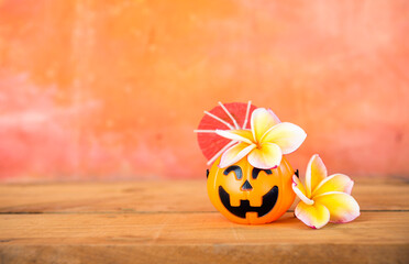 Halloween pumpkin with plumeria flower over blurred orange cement wall background, tropical Halloween card background idea