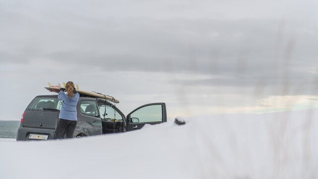 Woman removing surf board from roof of car