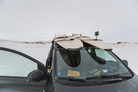 two surf boards on roof of small car in the snow
