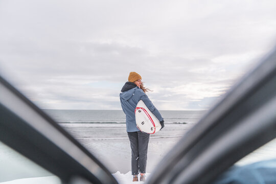 Woman standing in front of the ocean with surf board winter iceland