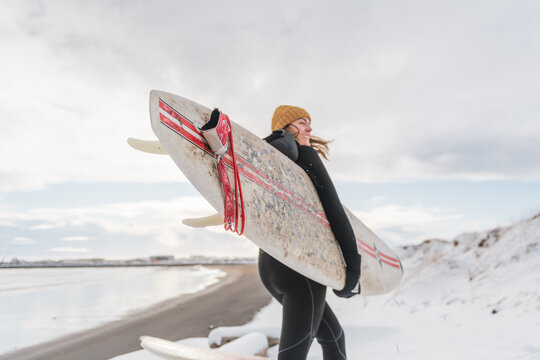 Woman walking on beach with surf board winter iceland