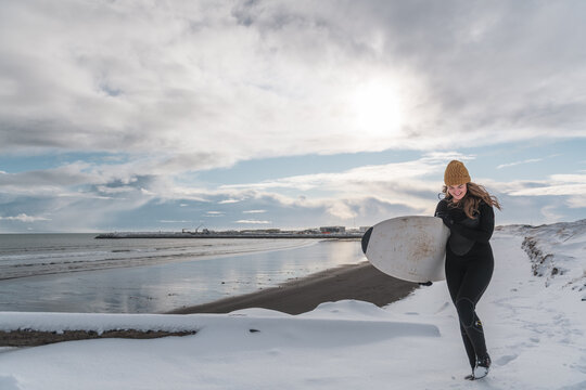 Woman walking on beach with surf board winter iceland