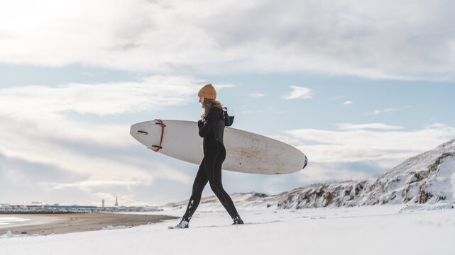 Woman walking on beach with surf board winter iceland