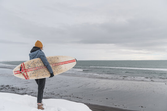 Woman standing in front of the ocean with surf board winter iceland