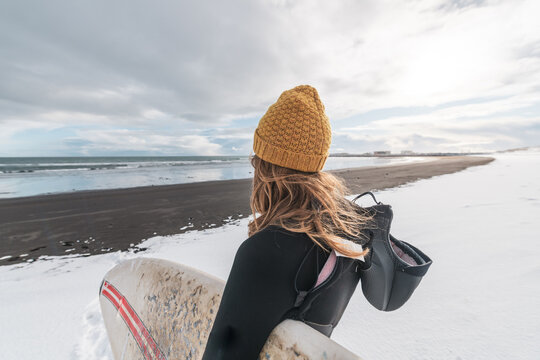 Woman standing on beach with surf board winter iceland