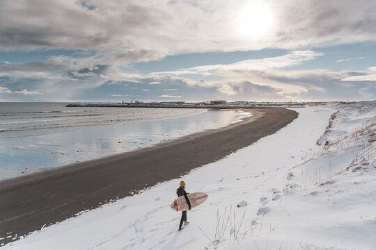 Woman walking on beach with surf board winter iceland
