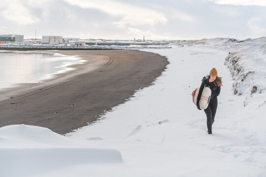 Woman walking on beach with surf board winter iceland