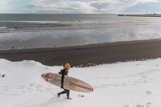 Woman walking on beach with surf board winter iceland