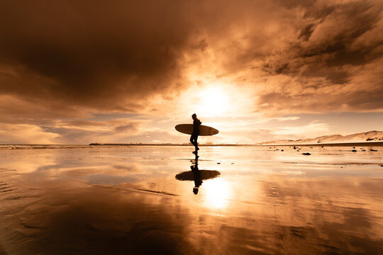 Woman standing on beach with surf board winter iceland sunset