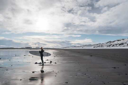 Woman walking on beach with surf board winter iceland