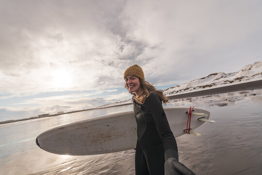 Woman walking on beach with surf board winter iceland