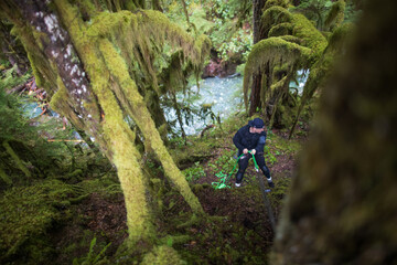 Adventurous man setting up rope for a rappel to a remote river