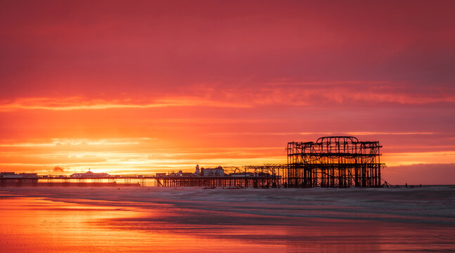 Brighton West  Pier and Palace Pier during a very vibrant red dawn on the east Sussex coast south east England UK
