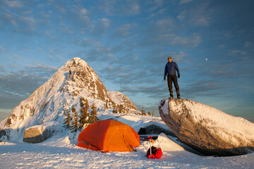 Mountaineer standing outside of tent below mountain summit