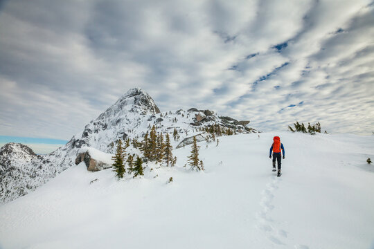 Hiker approaches mountain summit wearing snowshoes, leaving footprints
