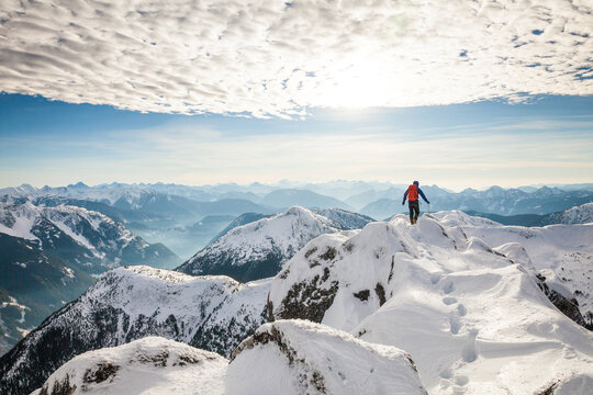 A hiker with backpack stands on the summit of a mountain in winter