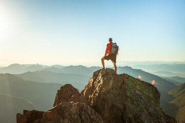 successful man stands on mountain summit at sunset