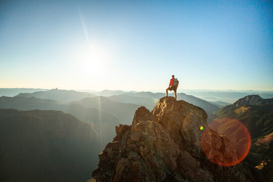successful hiker wearing backpack stands on mountain summit, sunset