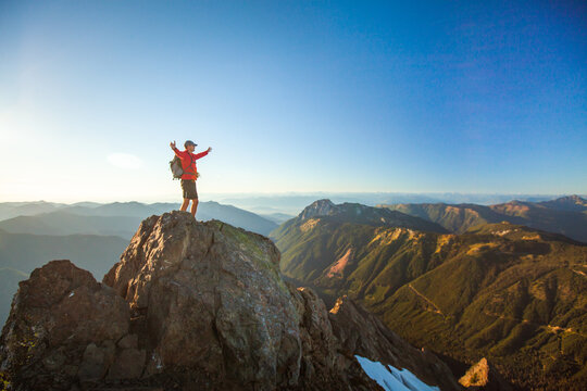 Successful hiker stands on summit with raised arms, scenic view