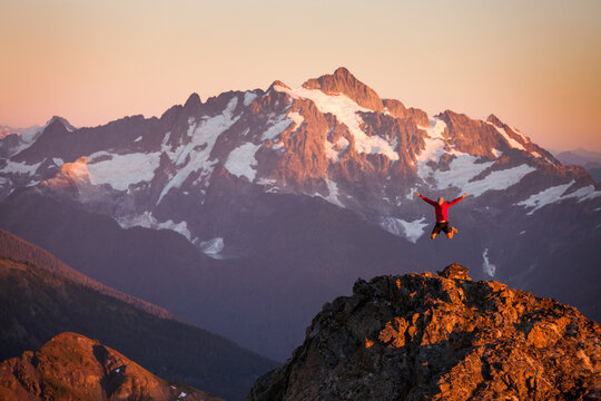 A hiker jumps off rocky cliff  in North Cascades National Park.