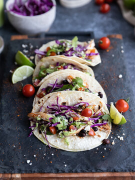 stacked tacos with colorful ingredients on dark background