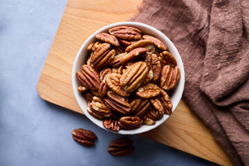 Top view, close-up of raw pecans in a bowl on the cutting board on gray background.