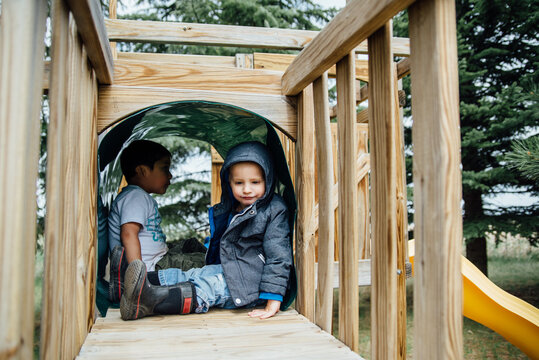Side view of two small boys sitting in tunnel of playground swing set.
