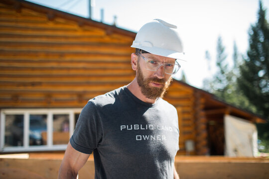 Bearded builder in safety gear by cabin.