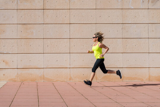 adult woman running along white pattern wall while doing workout