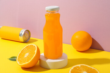 Glass bottle with juice, oranges and tin can on pink background