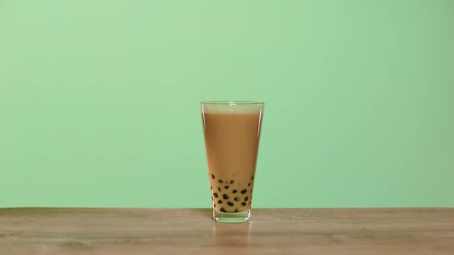 Hand stirring the milk bubble tea with a straw and removes the straw from the glass.
