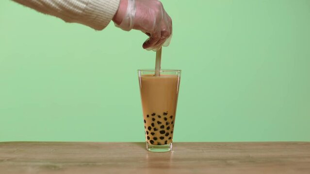 Hand stirring the milk bubble tea with a straw.