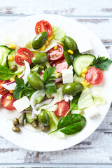 Healthy Salad with Feta Cheese, Green Olives, Baby Spinach, Cucumber, Cherry Tomatoes and Capers. Bright background. Top view. Close up.