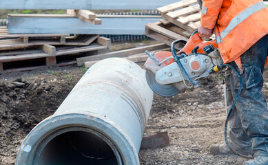 Construction worker cutting concrete pipe for drainage using a cut-off saw. Cutting concrete with a...