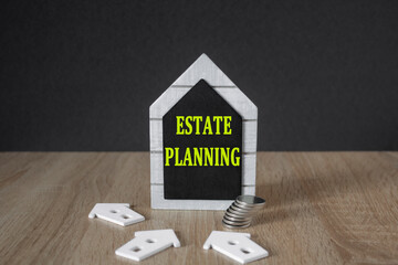 Estate planning symbol. Concept yellow words ESTATE PLANNING on a black board in the shape of a house near miniature houses. Beautiful wooden table. Business concept.