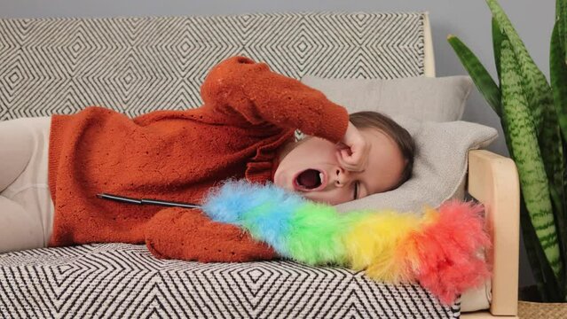 Sleepy little girl wearing brown sweater waking up after having rest lying on sofa with pp duster rubbing her eyes tired child working about the house and feeling fatigue