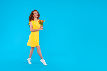 happy pleasedl smiling young woman in yellow dress  with bouquet of tulips posing against blue background with free space