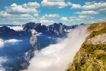 The picturesque stone trail PR 1 in Madeira. The route leads through rocky terrain, surrounded by lush greenery, under a blue sky with white clouds, creating a harmonious image of the island's natural