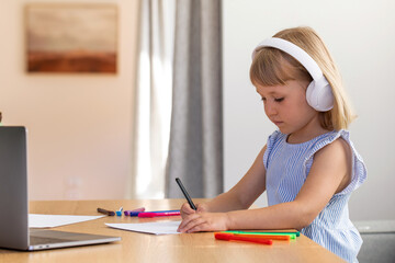  Online education. A girl with headphones listens to a teacher using a laptop at home. Education