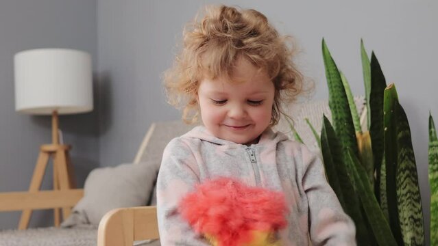 Funny laughing blonde wavy haired little toddler girl playing with pp duster having fun with cleaning tool helping with housekeeping chores and having fun