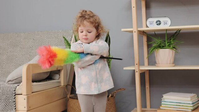 Cute adorable Caucasian toddler with pp duster in hands child little helper having fun at home household hygiene with kids domestic cleaning routine with infant helper