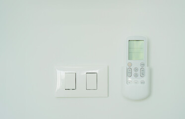 White electric switch and air conditioner remote control on the white wall.