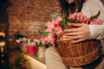 female florist holding wooden basket with pink tulips in flower shop
