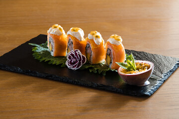 Salmon sushi roll dish garnished with creamy sauce and passion fruit, elegantly presented on a...