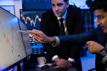 Two stock investors discussing and pointing interesting market stock on monitor. Trend of the...